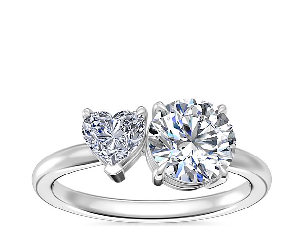 A heart-shaped diamond and round, princess or pear-cut diamond bring bold shimmer in this two-stone engagement ring design. The timelessly elegant design is crafted from lustrous 18k white gold that promises a bright gleam.