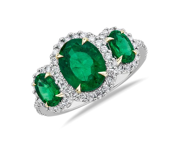 This romantic three-stone ring features oval cut emeralds surrounded by a shimmering diamond halo.  Yellow gold prongs add a dramatic flare to  what is already a show-stopping beauty.  Ring is a size 6.75.
