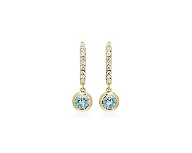 These gorgeous hoop earrings are beautifully crafted from lustrous 14k yellow gold. Shimmering diamonds line the front edge with eye-catching sparkle, and an aquamarine stone hangs elegantly from the bottom of each earring.