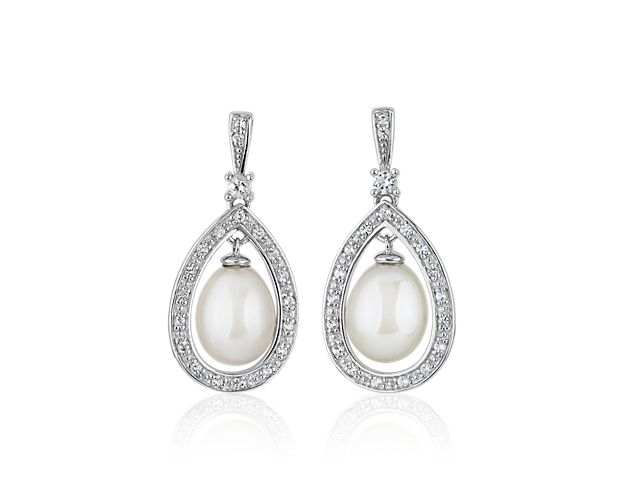 Indulge in elegance when you wear these drop earrings crafted from sterling silver. Each earring features a freshwater pearl surrounded by a pear-shaped halo of shimmering white topaz stones.