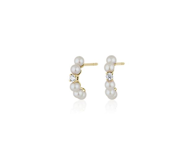 These timelessly elegant huggie hoops are crafted from gleaming 14k yellow gold. They feature a gleaming diamond centered on the front-facing edge, and flanked by two accent pearls on both sides.