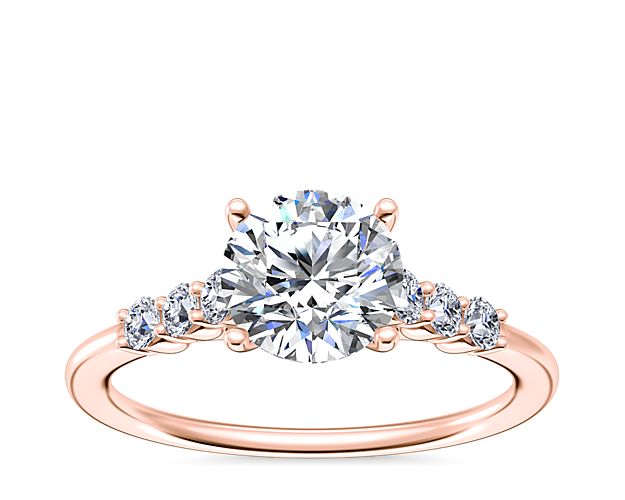 Beautifully designed in lustrous 18k rose gold, this cathedral engagement ring promises timeless romance. It features accent diamonds in shared prong settings trailing down the shank to add extra sparkle.