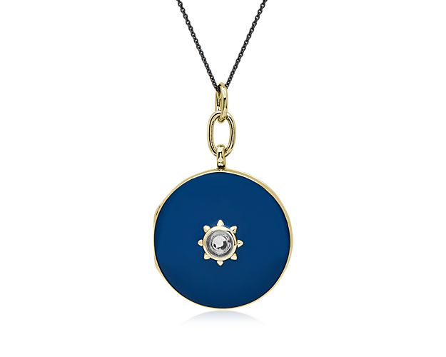 This round sterling silver locket features gleaming 18k yellow gold vermeil accented by dreamy blue enamel. A white topaz stone a the center is surrounded by a star bezel. It features a steel black cable chain.