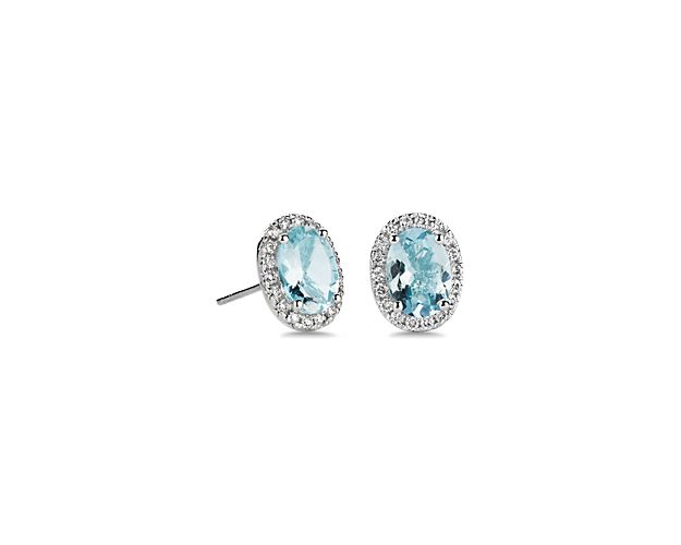 Crafted from lustrous white gold, these stud earrings feature oval-cut aquamarine stones that boast an eye-catching blue hue. Delicate diamonds surround each stone with a shimmering halo.