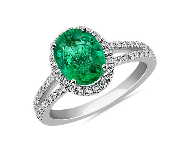 An oval-cut emerald nestles at the heart of this ring, capturing the eye with its dreamy green color. Accent diamonds sparkle in a bright halo around it and trail gracefully down the split shanks.