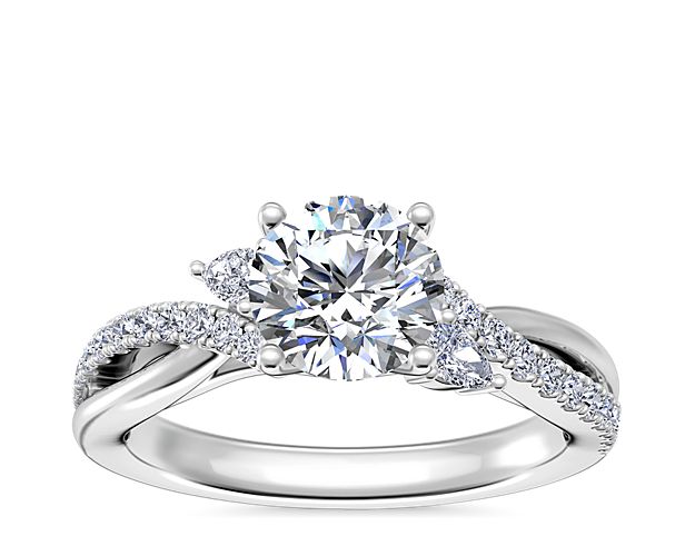 The gracefully entwining twist design of this gorgeous engagement ring is crafted in gleaming 14k white gold. The center diamond is completed by petal-like accent diamonds at the sides, and a trail of pavé-set diamonds accents one arm of the twisting split shank.