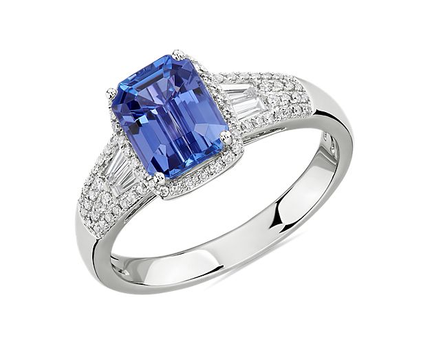 This ring showcases an emerald-cut tanzanite gemstone accented by baguette sidestones and framed with sparkling round diamonds in 14k white gold.