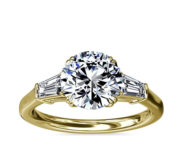 A timeless symbol of love and beauty, this 18k yellow engagement ring marries Art Deco-inspired style with pure elegance as twin tapered baguette diamonds frame a center stone casting their everlasting light in every direction.