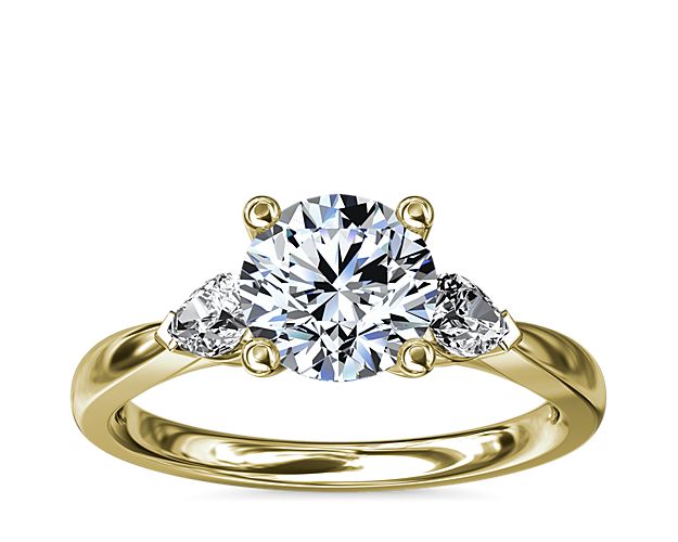 A delicately curved yellow gold setting embraces your precious diamond while pear-shaped side stones add a fancy-cut edge.