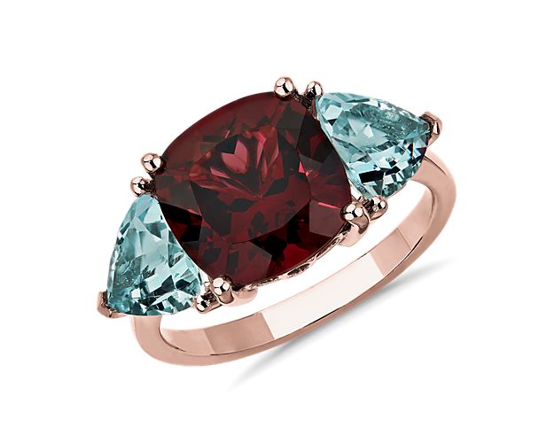 Artful floral settings punctuate the romantic look of this rose gold ring crowed by a duo of trillion-cut aquamarine set on either side of a statement-making cushion-cut rhodalite.