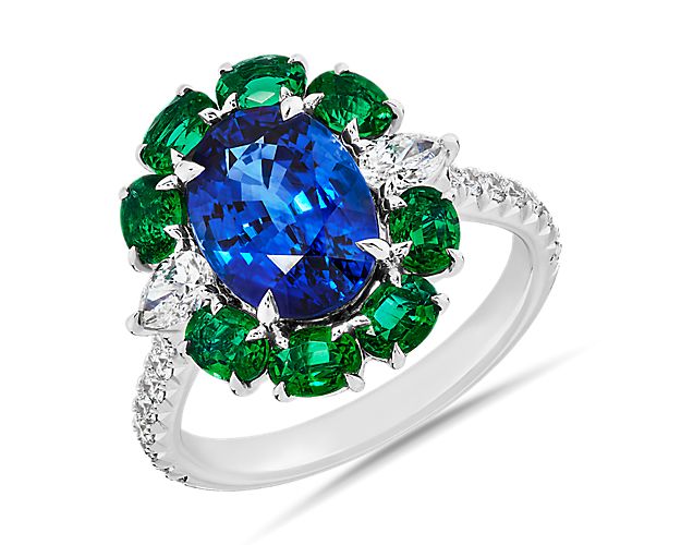 Find floral delight in the petal-like pattern of this 18k white gold ring. Diamonds accent the polished band while eight oval emeralds encircle the show-stopping blue sapphire in the center.  This ring is accompanied by gemstone report #:CDC1910585.