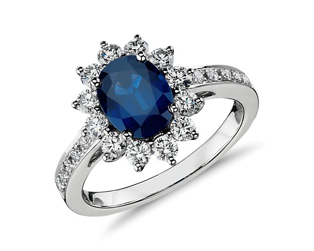 Put high style on her finger with this iconic oval sapphire and diamond ring. A statement-making deep blue faceted oval sapphire is encircled by round brilliant-cut diamonds set in traditional 18k white gold. Petite diamonds across the shoulders of the band add an extra dose of sparkle. A beautiful alternative to a diamond engagement ring.