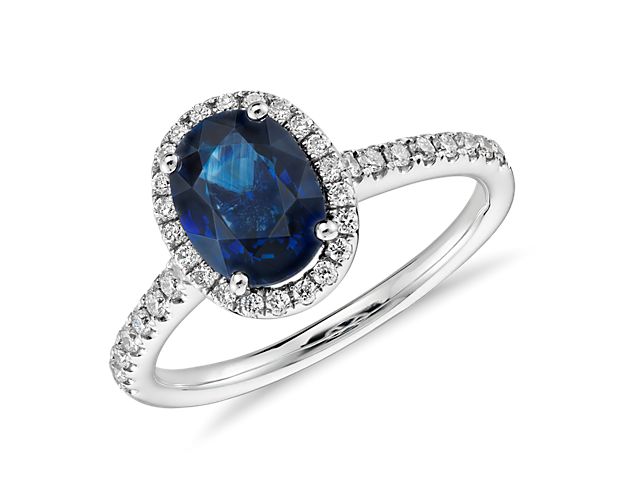 A shimmering blue oval sapphire gemstone rests elegantly in a halo of stunning micropavé diamonds set in 14k white gold.