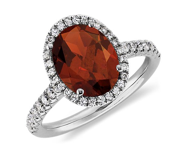 A vision of color, this garnet and diamond halo ring features a fiery red oval garnet gemstone framed by a halo of pavé set round brilliant diamonds set in polished 18k white gold.