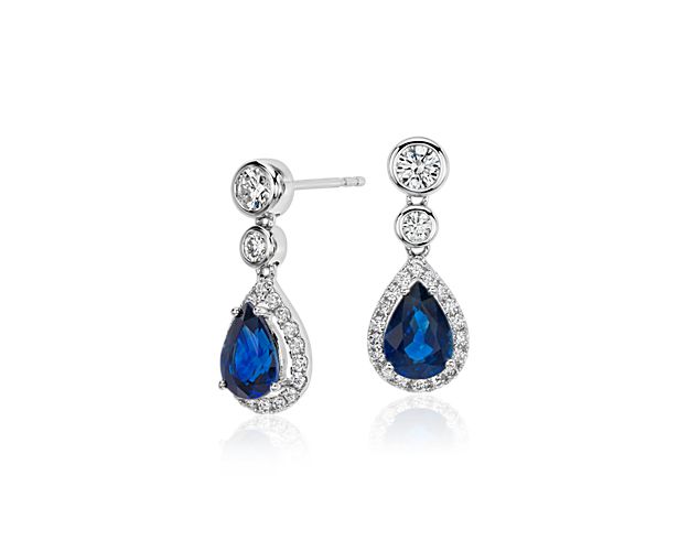 Timeless elegance gains a touch of color in these dazzling dangle earrings, showcasing vibrant pear-shaped sapphire gemstones surrounded by halos of round brilliant diamonds set in 18k white gold.