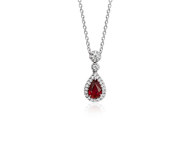 Crafted to reflect sophisticated elegance, this timeless drop pendant showcases a vibrant pear-shaped ruby gemstone framed by a delicate halo of pavé-set diamonds set in 18k white gold.