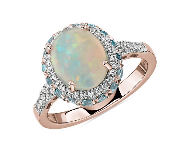 A vision of radiant beauty, this 14k rose gold ring is splendidly crafted with a vibrant oval opal framed by a double halo of blue topaz and white sapphires that cascade down the band. While perfect for special occasions, opals are a softer gemstone and not recommended for daily wear.