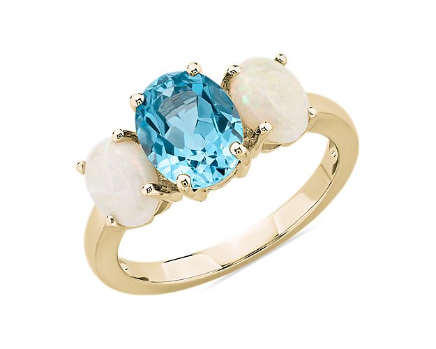 Refined elegance defines the captivating look of this 14k yellow gold ring centered by an oval Swiss Blue topaz stone with two iridescent oval opals hugging it on either side.