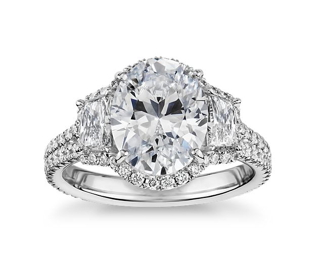 The oval-shaped center stone of your choice sits at the center of this breathtaking platinum ring and is flanked by dazzling trapezoid diamonds and surrounded by a brilliant pavé halo.