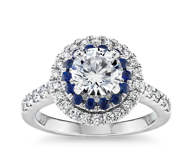 Like putting your diamond on a pedestal of gemstones, this spectacular design lifts your diamond and surrounds it with a halo of sapphires, then another halo of diamonds, with more diamonds cascading along the white gold band.