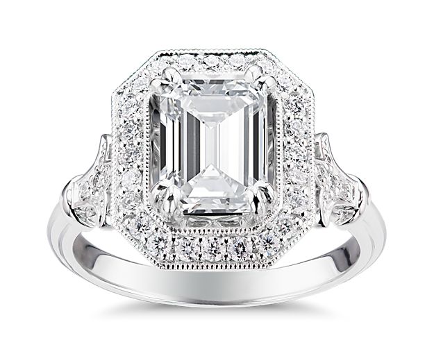 There's so much to love with this vintage-inspired engagement ring. An emerald-cut center stone of your choice is surrounded by a halo of 20 round brilliant diamonds, encircled by a delicate trail of milgrain accents, and flanked on either side by Fleur de Lis motifs adorned with pavé diamonds.