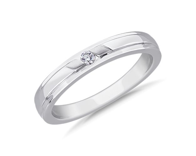 Simple yet sleek, a round brilliant cut diamond is set in the center of this platinum ring with inlayed grooves along each edge.