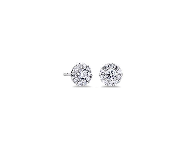 Lend a touch of sparkle to your look with these classic stud earrings each featuring a round-cut diamond encircled with a stunning diamond halo. They are designed in lustrous 14k white gold for enduring quality and beauty.