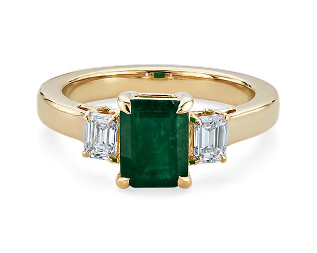 A gorgeously green emerald-cut emerald takes centre stage in this stunning ring, with an emerald-cut accent diamond on either side of it. It is crafted in warmly lustrous 14k yellow gold to complete the elegant effect.